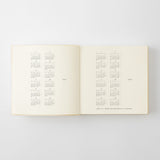 An open cream-colored  diary showing printed calendar grids on both pages, photographed against a light gray background.