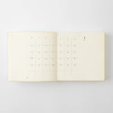 An open cream-colored diary showing a minimalist monthly calendar grid on the left page and the date '1 Jan' on the right page, photographed against a light gray background.