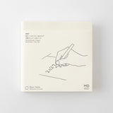 A square cream-colored notebook or planner cover with minimalist black line art of a hand writing '2027' and small printed text, shown against a light gray background.
