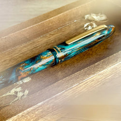 Fountain pen with a decorative blue and gold design on a wooden surface