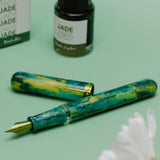 Green and gold fountain pen with 'Jade' ink bottle and packaging on a green background