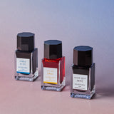 Three ink bottles with black caps and clear bodies on a gradient background
