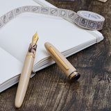 Fountain pen and ink bottle on an open notebook with decorative tape on a wooden surface