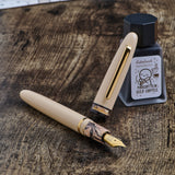 Fountain pen and ink bottle on a wooden surface with a notebook in the background